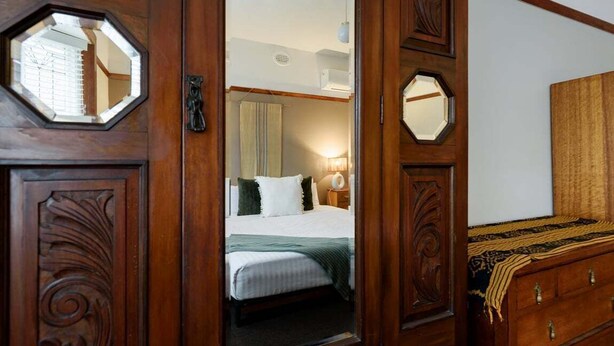 Una puerta de madera con un espejo y vista a un dormitorio con cama, mesita de noche y cómoda.