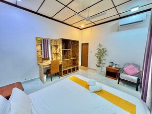 A hotel room with a bed, a desk, a chair, a small table with a plant, and an air conditioning unit. - Bella Stay Inn Fvm (Fuvahmulah)