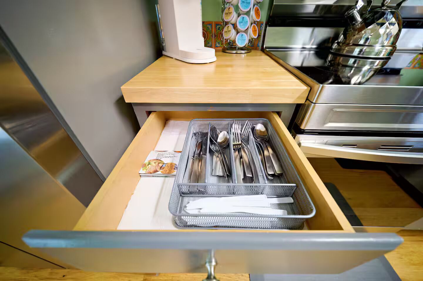 A kitchen drawer with utensils and a cookbook.