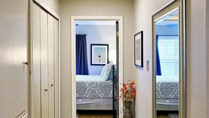 Ein Flur mit Holzboden, einem gemusterten Teppich, einem Spiegel und einer Tür, die in ein Schlafzimmer mit Bett und Fenster führt.