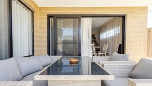 Un espacio moderno para sentarse al aire libre con una mesa de vidrio y muebles de mimbre.
