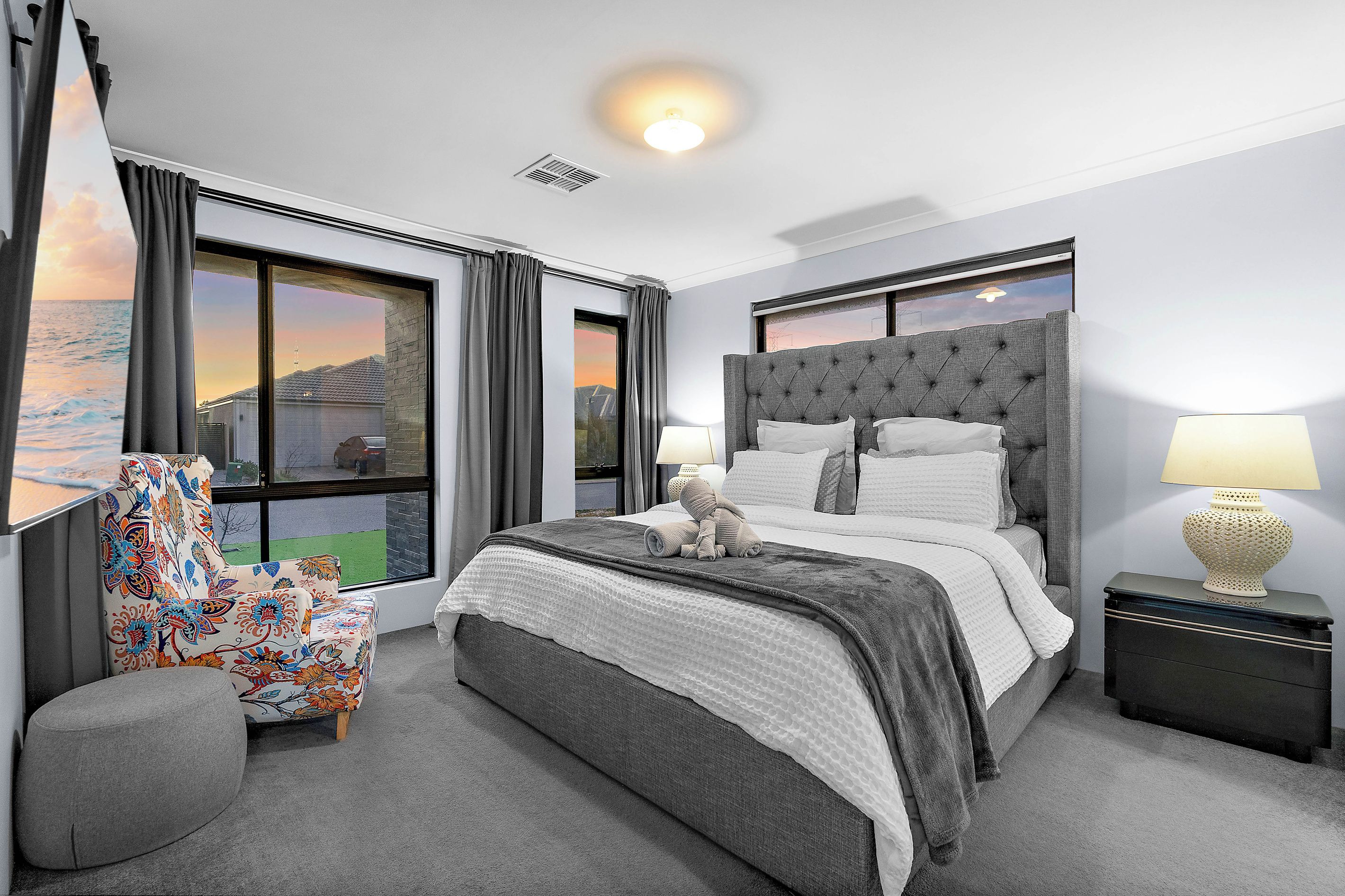 A modern bedroom with a large bed, a view of the sea through the window, and a nightstand with a lamp.