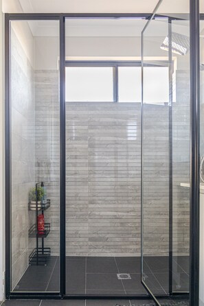 A modern shower area with a glass door, tiled walls, and a small shelf with toiletries. - Spacious 4BR Home | Near Murdoch & Freo (Success)