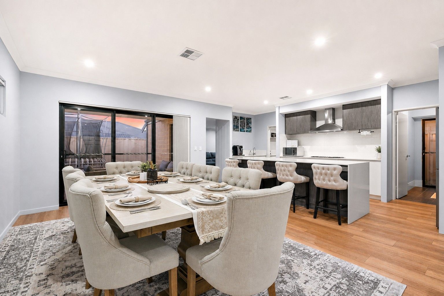 A modern kitchen with a central island, a dining area with a table set for six, and a large window with a view.