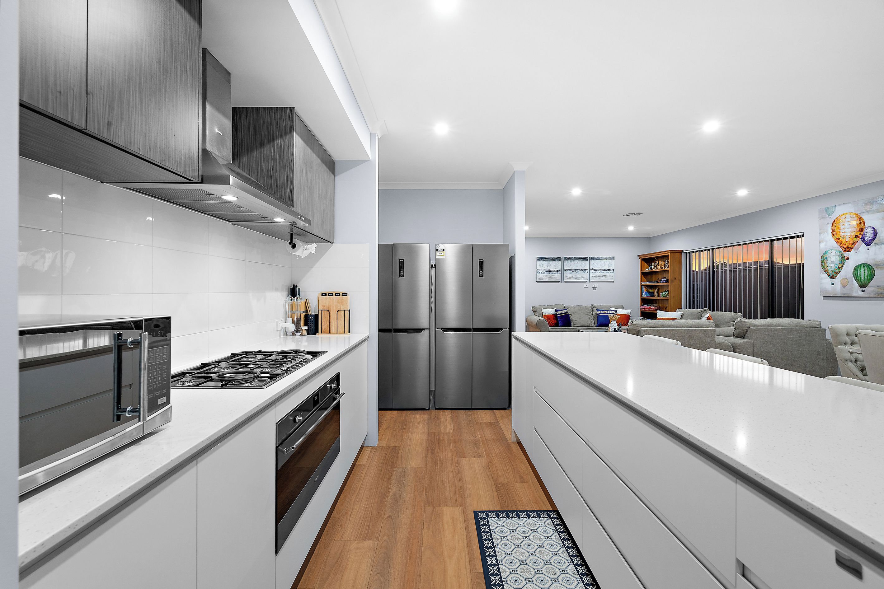 A modern kitchen with stainless steel appliances, white cabinetry, and a wooden floor.