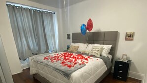 Une chambre à coucher avec un lit, un ventilateur de plafond, une table de chevet et une fenêtre avec des rideaux.