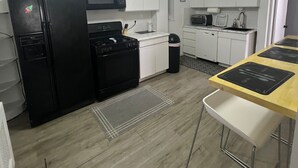 Une cuisine moderne avec des meubles blancs, un réfrigérateur noir, un four à micro-ondes, une cuisinière et un ventilateur de plafond.