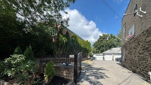 Une allée menant à une résidence, avec un mur en briques, un portail en métal et un garage.