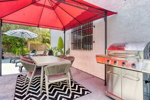 Eine Terrasse im Freien mit Grill, Esstisch, Stühlen und einem roten Sonnenschirm.
