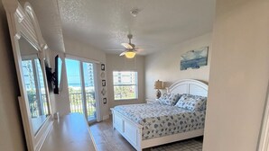 A bedroom with a bed, a dresser, a ceiling fan, and a window with a view. - Ocean Walk Condo: Classy Beachy Retreat in charming New Smyrna Beach (New Smyrna Beach)