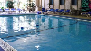 En inomhuspool med klart vatten, blå solstolar och ett område vid poolen med stolar och bord.
