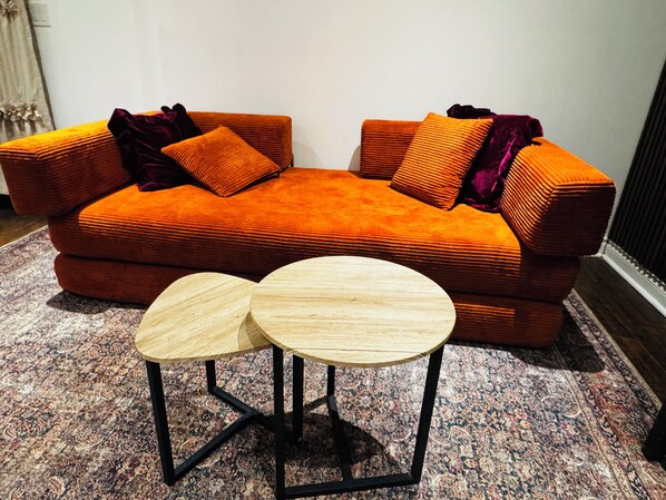 Un sofá moderno naranja con cojines a juego y una pequeña mesa de madera al frente.