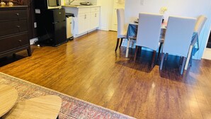 Una cocina moderna con armarios blancos, un refrigerador negro y un microondas. Hay una zona de comedor con una mesa y sillas, y una alfombra estampada en el suelo.