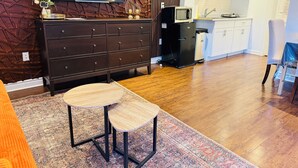 Una sala moderna con un mueble de madera oscura, un televisor de pantalla plana, una pequeña cocina con microondas y una mesa de comedor con sillas.