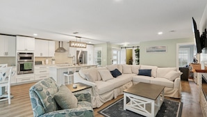 A modern living room with a sectional sofa, a coffee table, and a dining area with white cabinets and a kitchen in the background. - Tee to Sea Retreat - Inside TPC Sawgrass Gated Community, Ponte Vedra Beach  (Palm Valley)