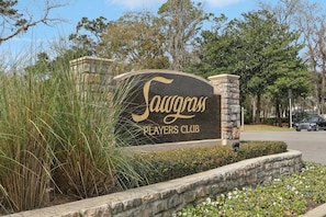 Schild für den Sawgrass Players Club mit einer Steinsäule und einer angelegten Grünfläche mit Gras und Blumen.