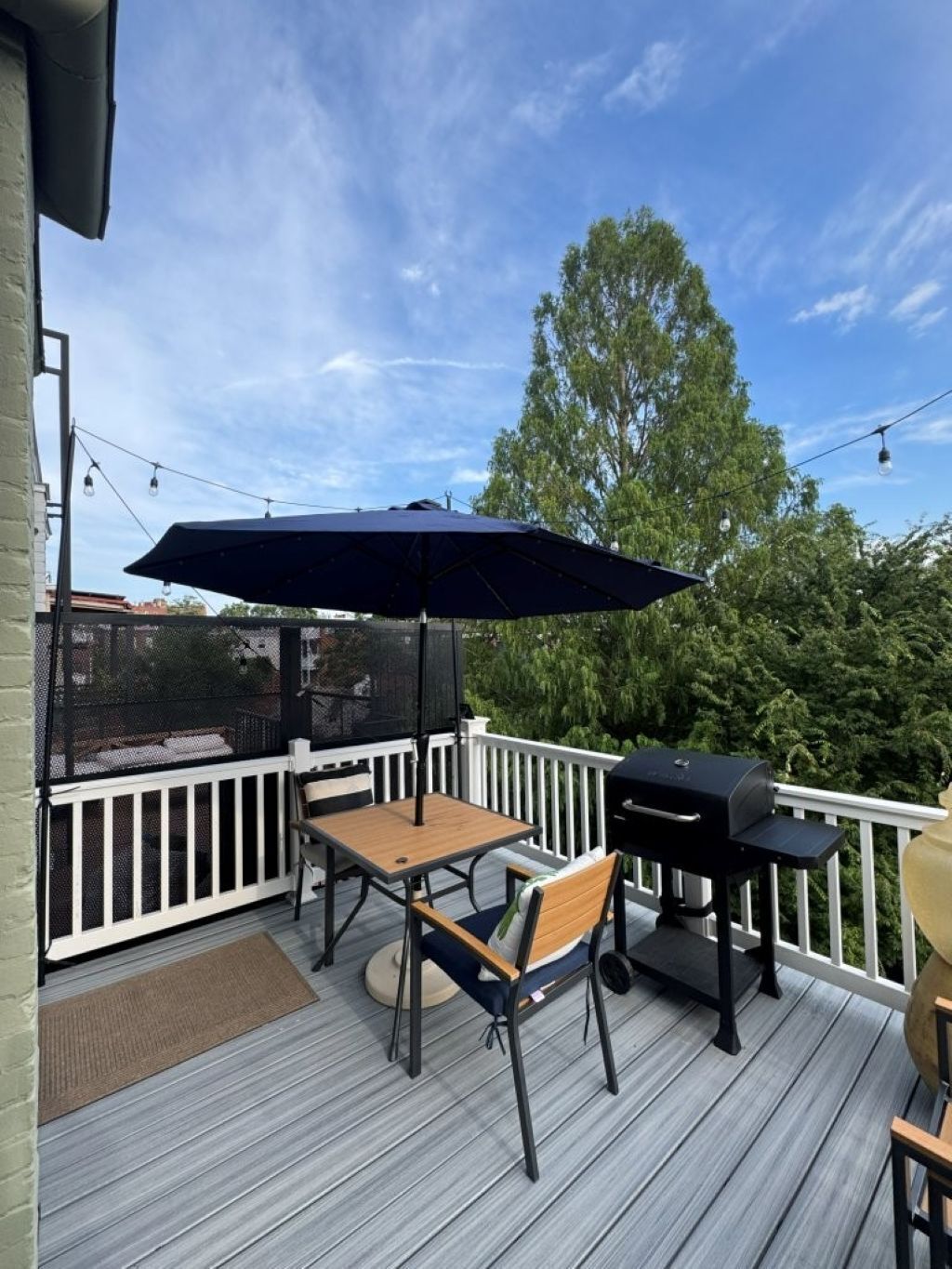 Une terrasse avec une table et des chaises, un barbecue et un parasol.