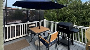 Een terras met een tafel, stoelen, een barbecue en een parasol.