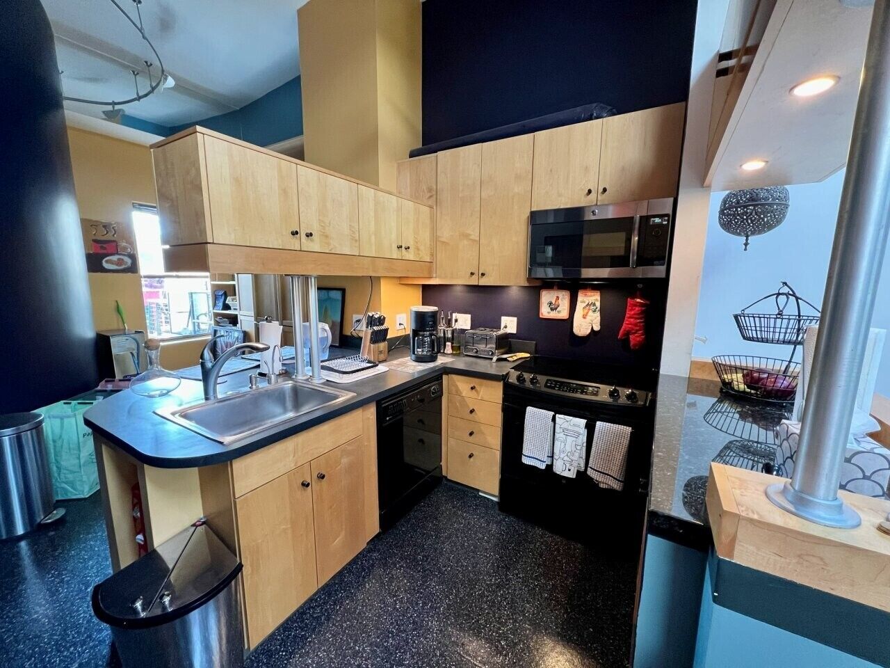 Une cuisine de taille réduite, avec des meubles de rangement en bois, une cuisinière noire et un four à micro-ondes.
