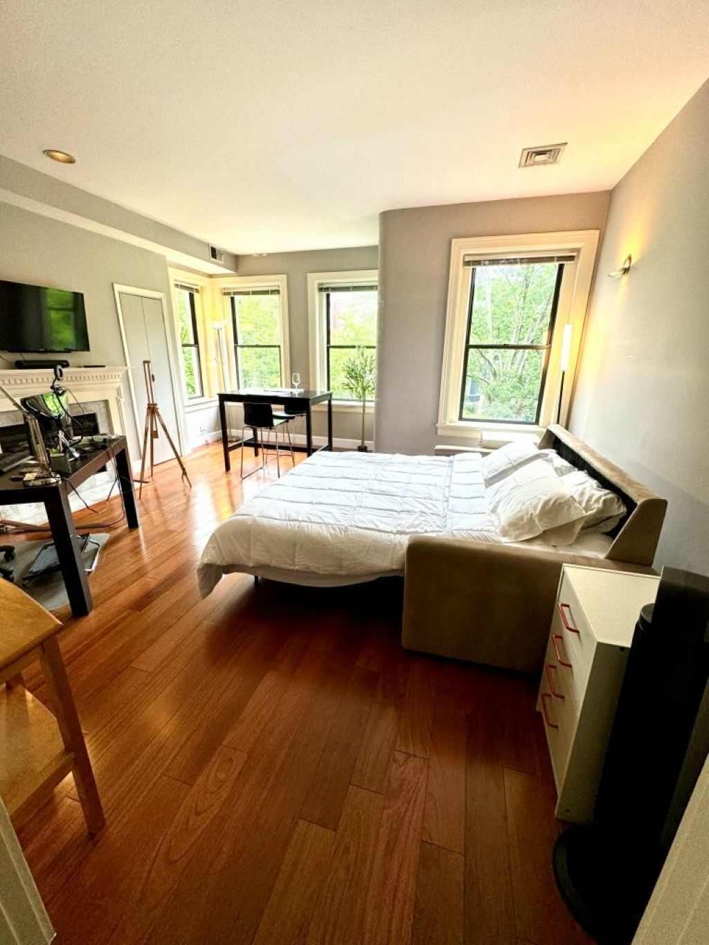 Une chambre avec un grand lit, un bureau et une chaise. Il y a des fenêtres et un téléviseur au mur.