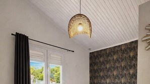 Un dormitorio con cama, ventana con cortinas, pared con diseño, lámpara colgante y una planta.