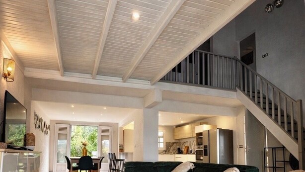 Un amplio espacio habitable con techo alto, una escalera y una cocina al fondo.