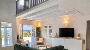 Amplia sala de estar con un sofá seccional verde, un televisor de pantalla plana y un balcón con plantas en macetas.