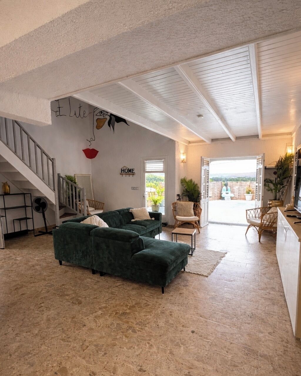 Amplia sala de estar con un sofá verde, una escalera y vistas al exterior.