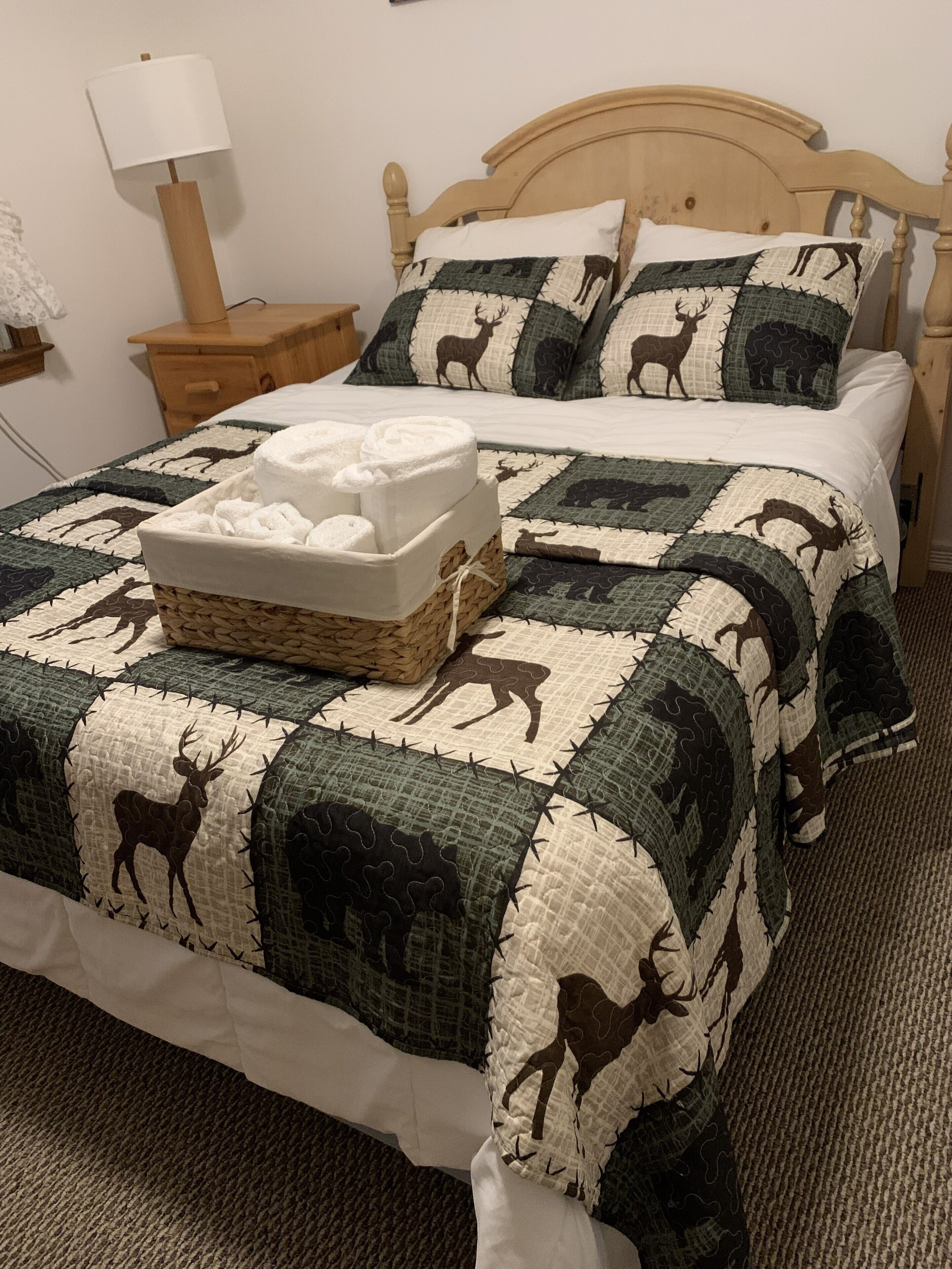 Ein ordentlich bezogenes Bett mit einer Zudecke mit Tiermotiven, ein Nachttisch mit Lampe und eine Nachttischschublade.