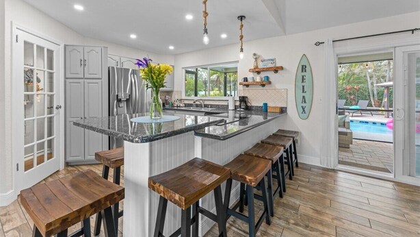 A modern kitchen with a central island, bar stools, and a view of an outdoor pool. - Private Palm Harbor Home H/Pool, Hot Tub, Tiki Bar, Putting Green and More! (Palm Harbor)