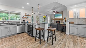 A modern kitchen with grey cabinets, a wooden island with stools, and a large window overlooking greenery. - Private Palm Harbor Home H/Pool, Hot Tub, Tiki Bar, Putting Green and More! (Palm Harbor)