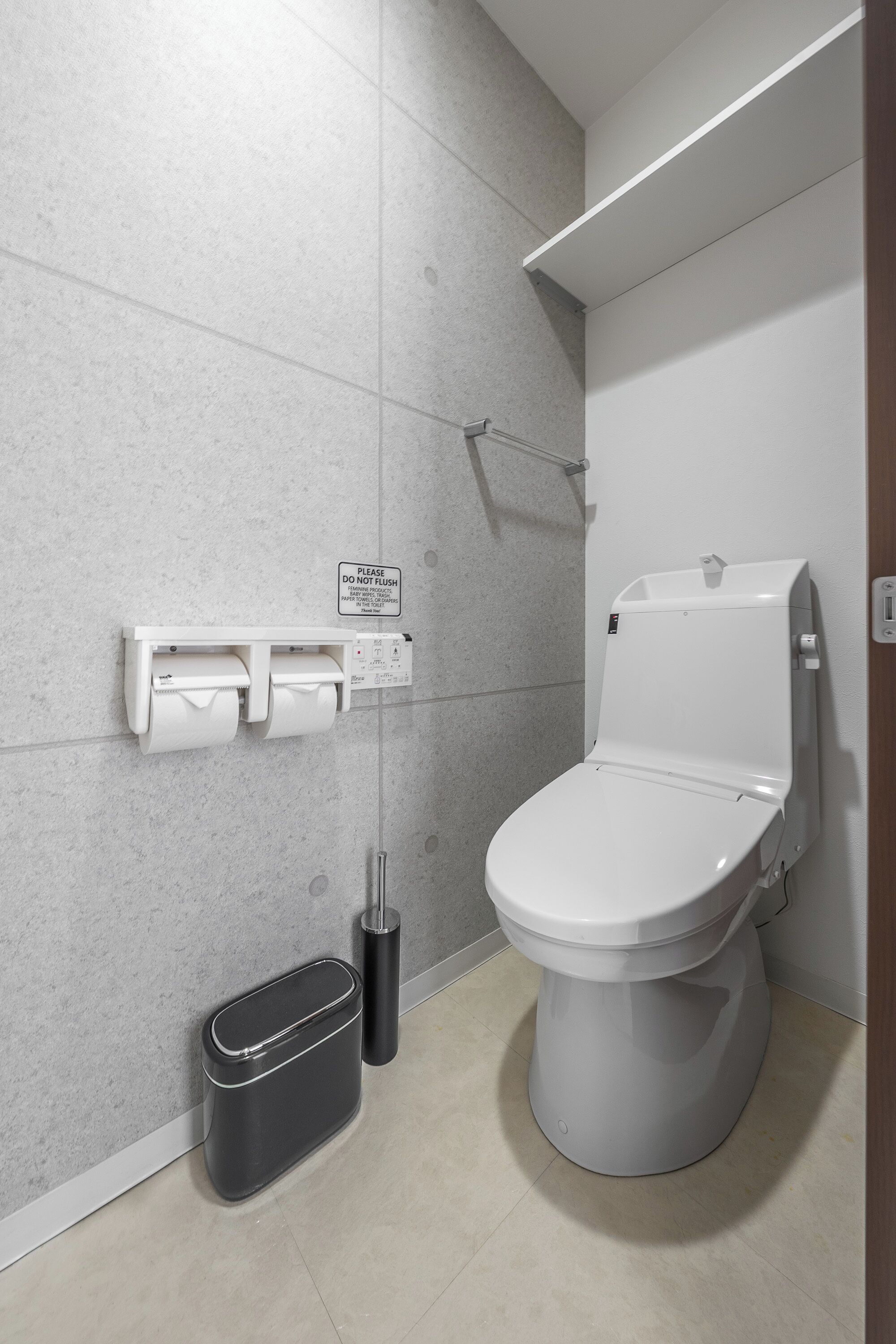 A modern bathroom with a toilet, a trash bin, and a paper towel dispenser.