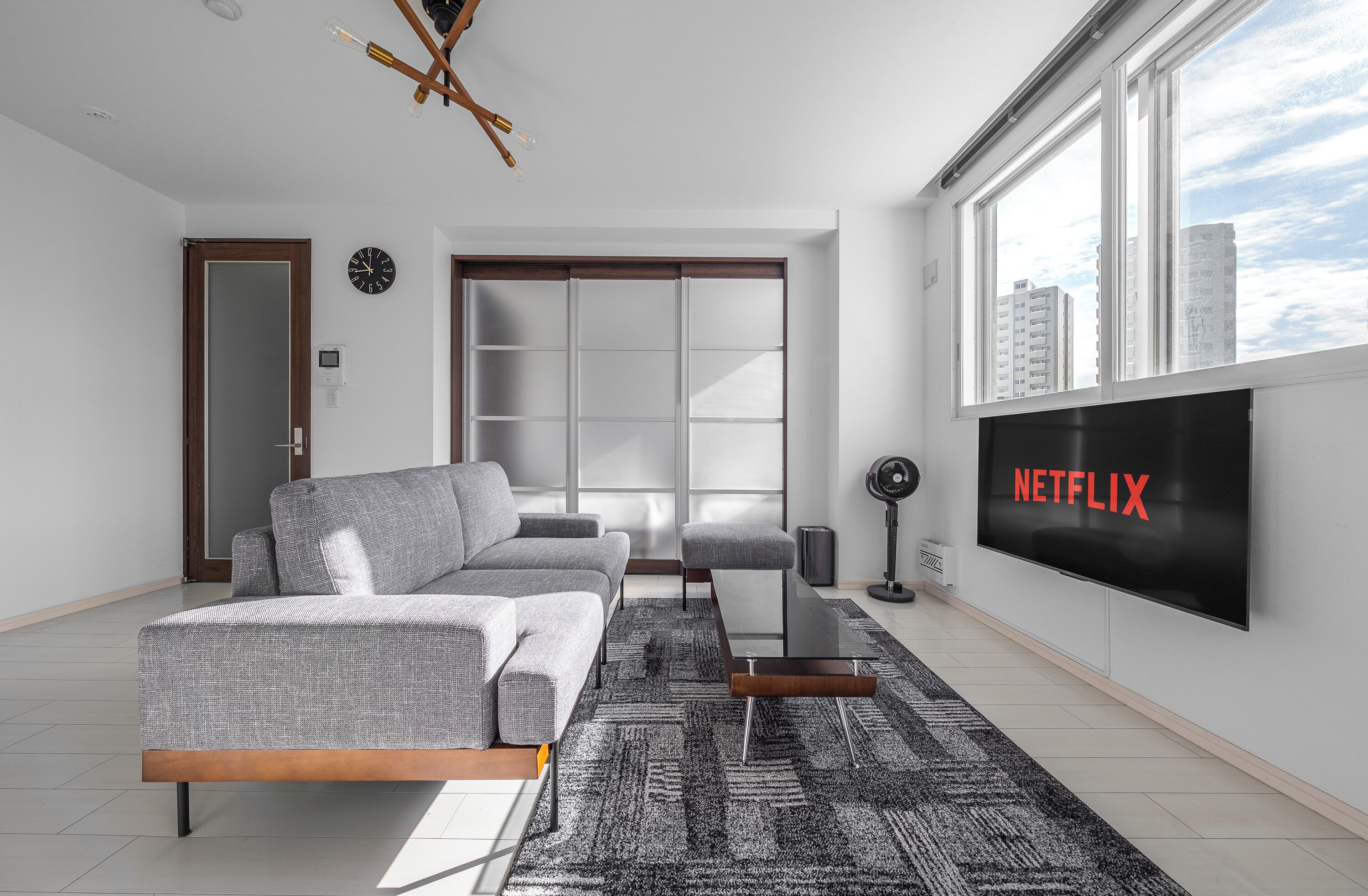 A modern living room with a grey sofa, a coffee table, and a large flat-screen TV displaying 'NETFLIX'.