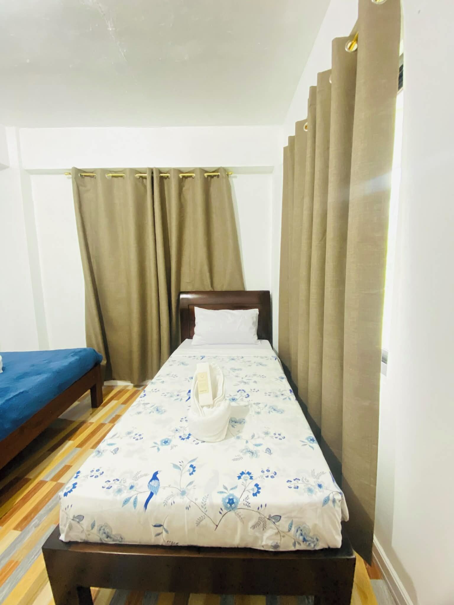 Un lit simple avec une couvre-lit à motifs floraux, une tête de lit en bois et un matelas bleu, situé à gauche.