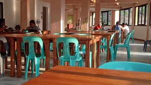 A dining area with wooden tables and turquoise chairs, large windows, and indoor plants. - Australian Hotel Hungduan (Hungduan)