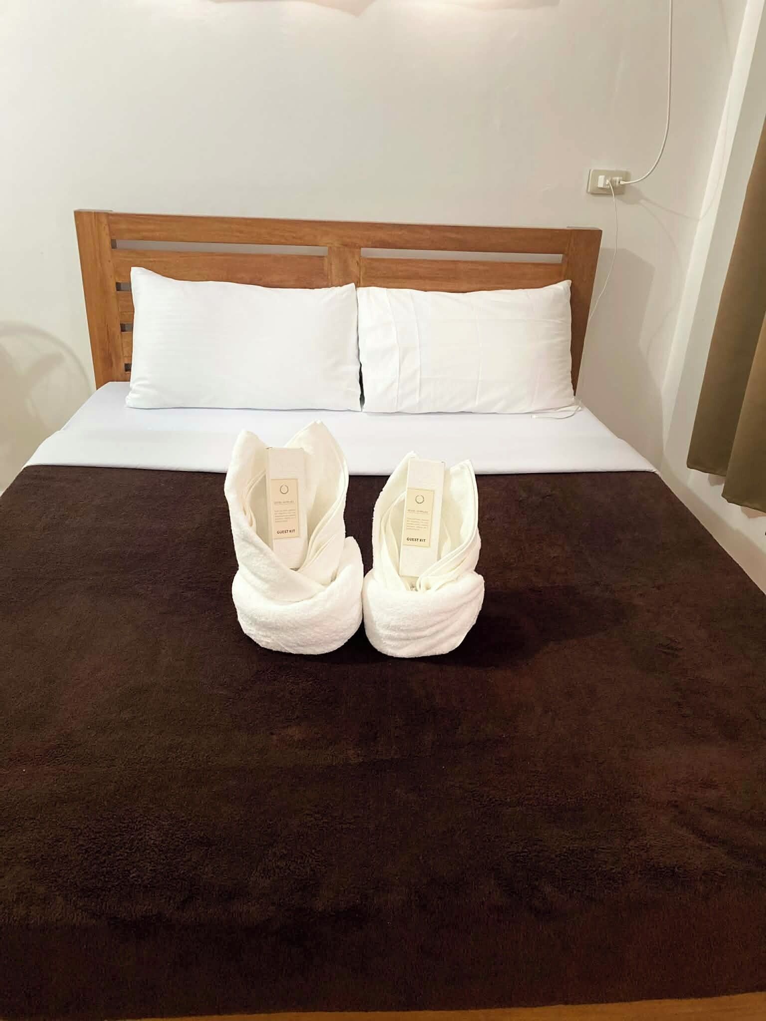 A bed with a dark brown bedspread, two white pillows, and two white towels placed on the bed.