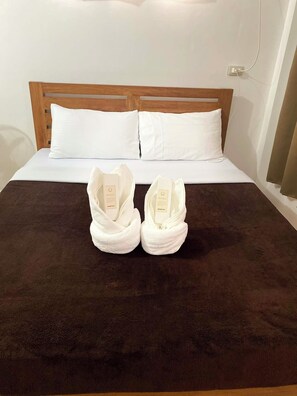 A bed with a dark brown bedspread, two white pillows, and two white towels placed on the bed.