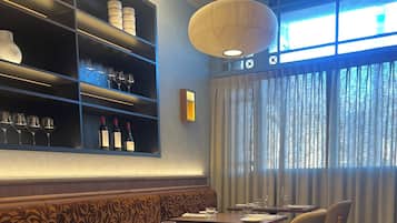 A restaurant interior with a long dining table, chairs, and a bar area with shelves.