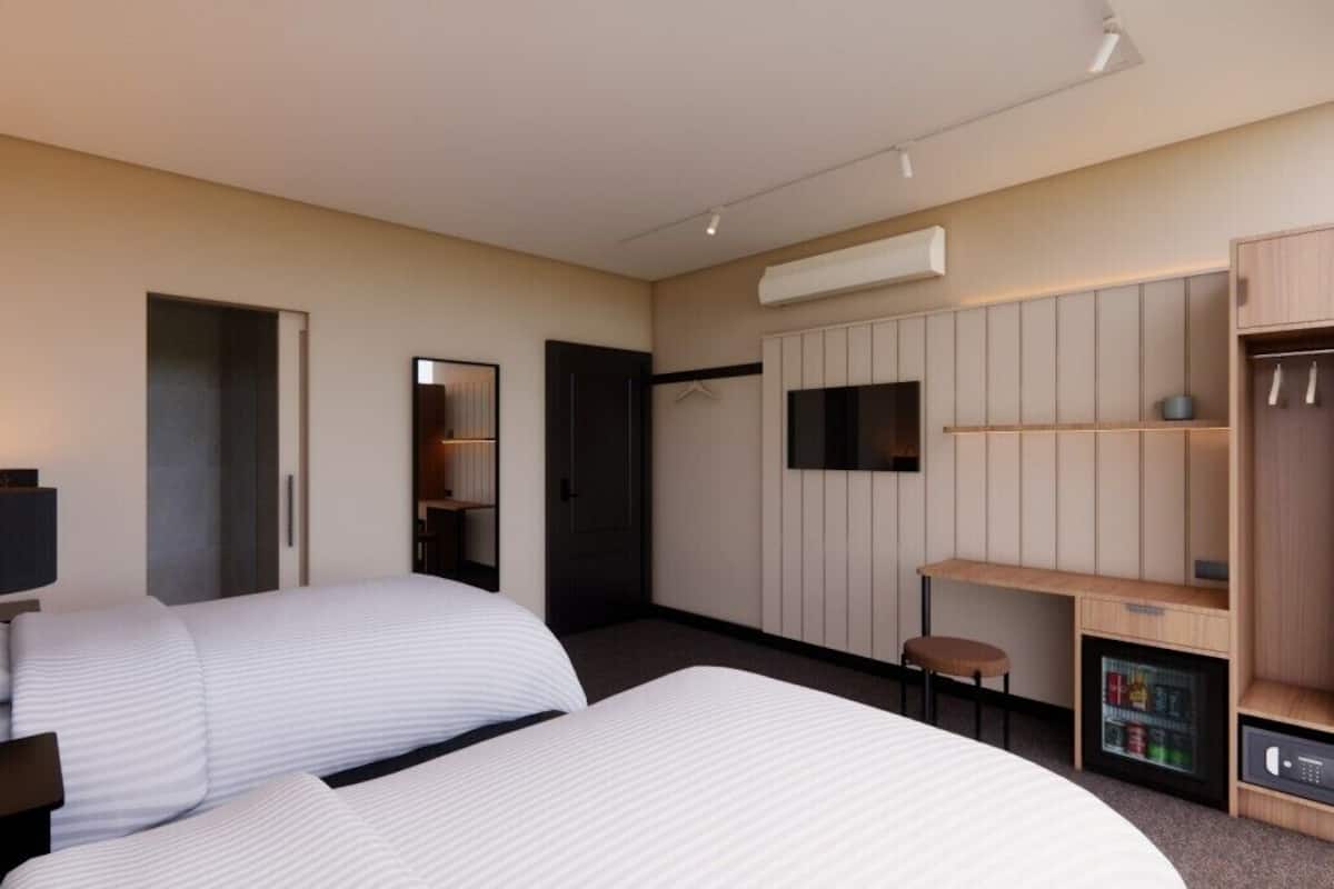 Habitación de hotel con dos camas, un escritorio, un armario, televisión y un minibar.