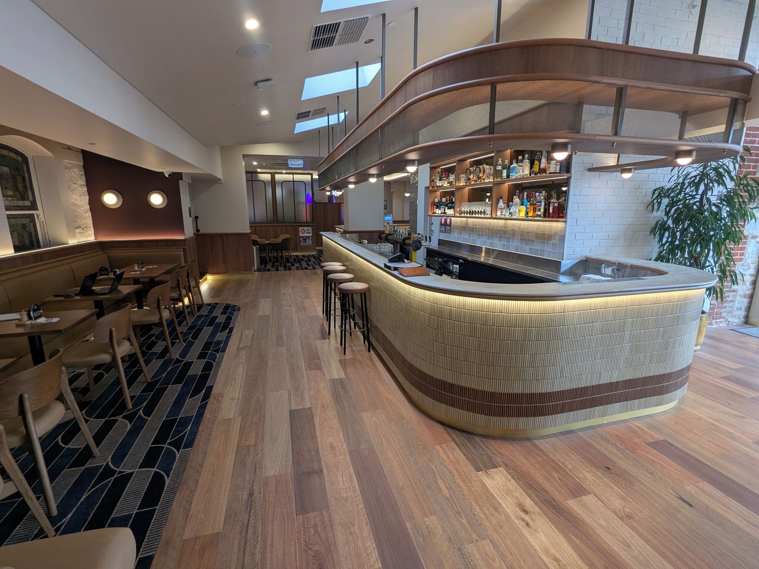 Zona de bar moderna con mostrador curvo, asientos y cocina a la vista.