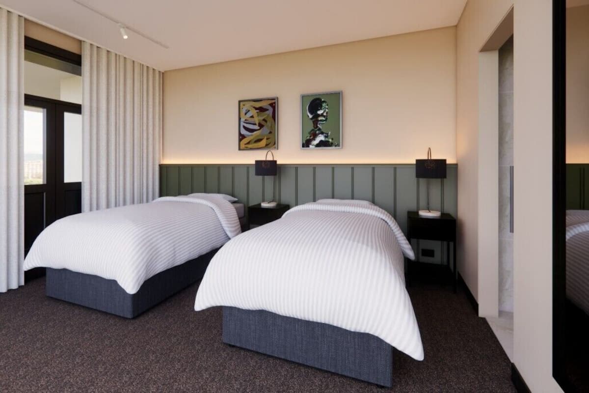 Habitación de hotel con dos camas, un ventanal con cortinas, un televisor montado en la pared y dos obras de arte enmarcadas.
