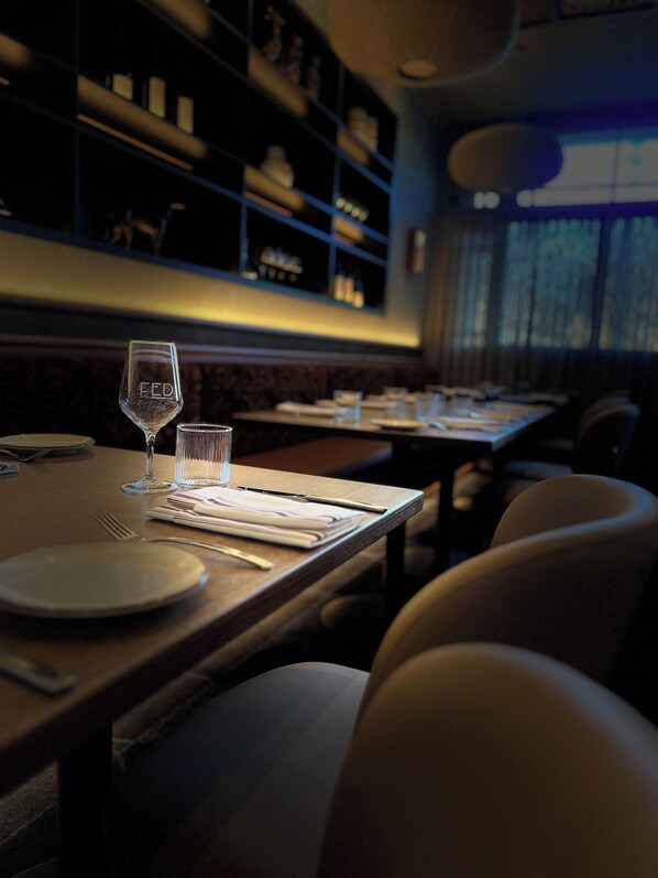 L’intérieur d’un restaurant, avec des tables dressées pour le service, de la vaisselle en verre transparente et un design moderne.