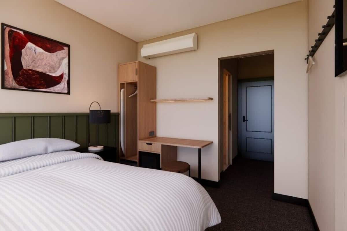 Una habitación de hotel con una cama, un escritorio, un armario y una puerta que da a otra habitación.
