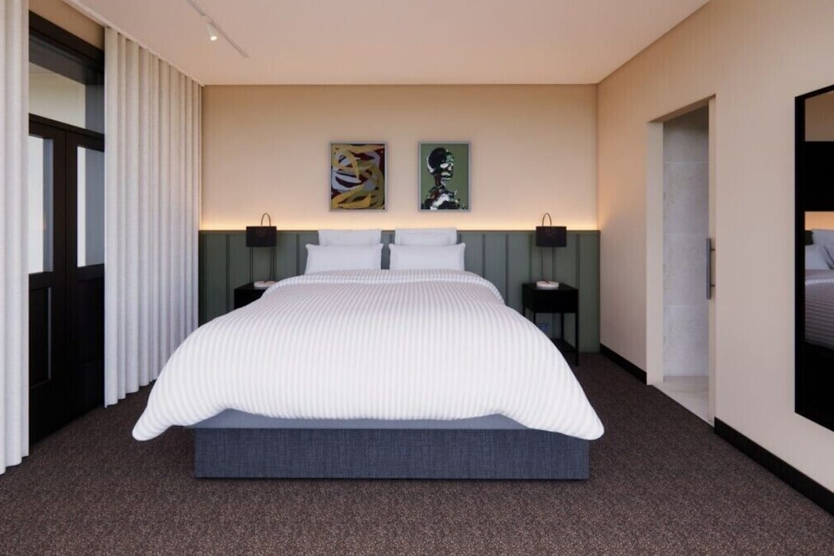 Una habitación de hotel moderna con una cama grande, dos mesitas de noche, un televisor montado en la pared y una obra de arte sobre la cama.