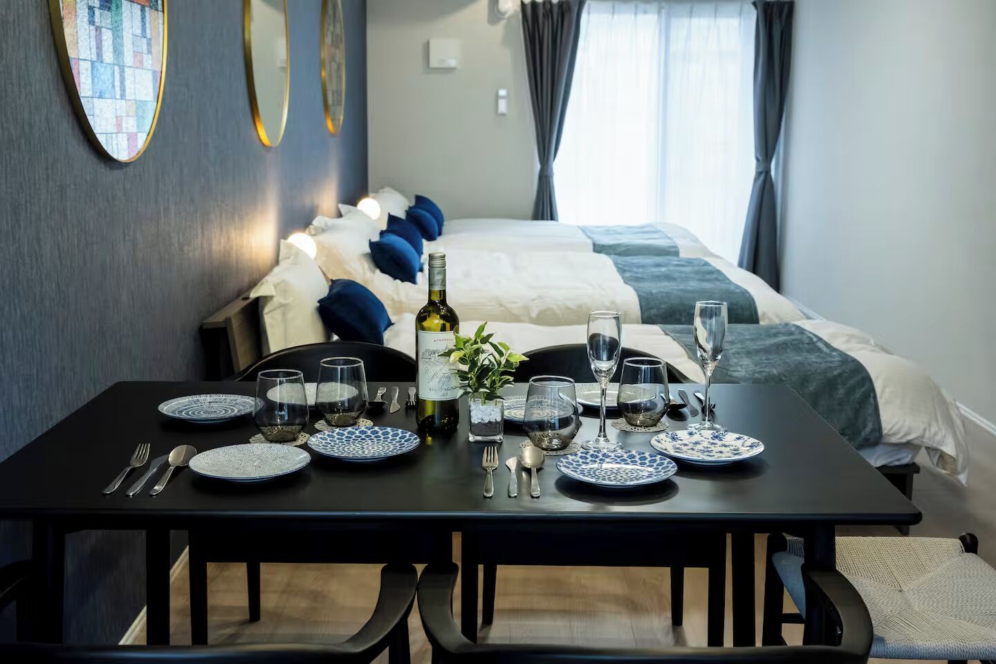 A neatly set dining table with plates, glasses, and cutlery, a bottle of wine, and a potted plant.