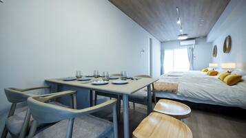 Une pièce compacte comprenant une table à manger pour quatre personnes, un lit avec des coussins jaunes et un petit coin salon.