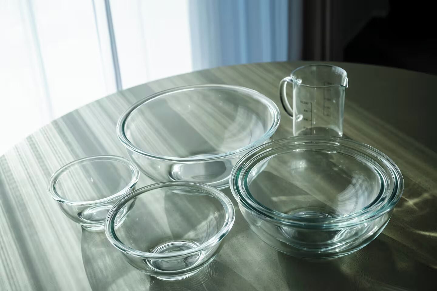 Un ensemble de verres à mesurer en verre transparent et un pichet, le tout posé sur une surface réfléchissante.