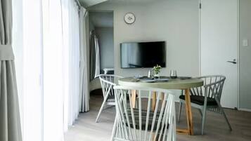 Una habitación moderna con una mesa de comedor redonda, sillas blancas, un televisor de pantalla plana en la pared y una puerta.