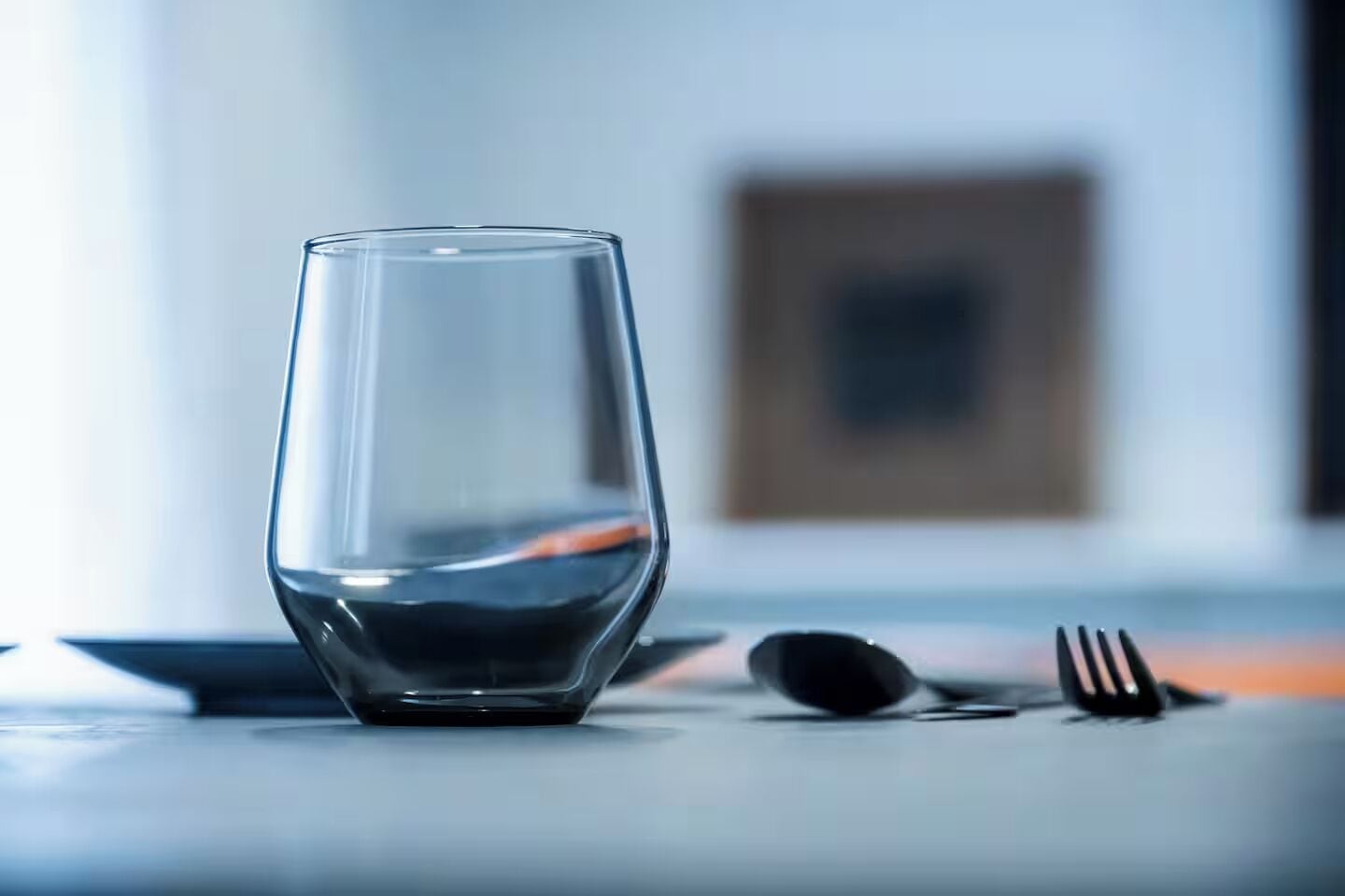 Un verre transparent posé sur une table, avec une fourchette et une cuillère à côté.