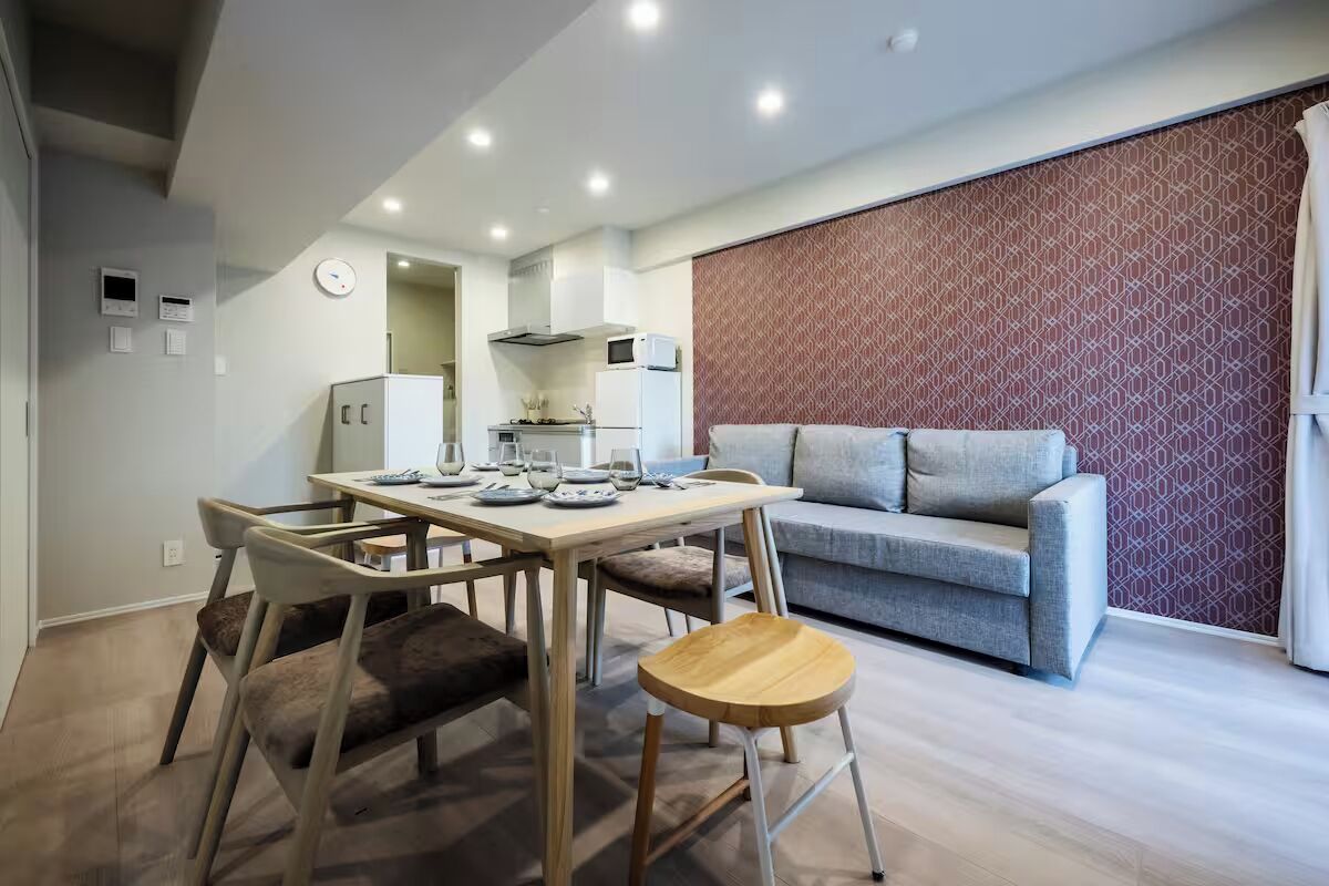 A modern living room with a sofa, a dining table with chairs, and a kitchen area in the background.